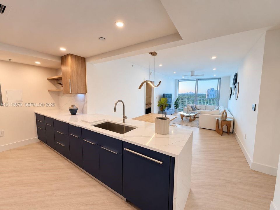 Kitchen featuring navy blue lower cabinetry, white stone countertops, wood-finish cabinetry accents, recessed lighting, and a stainless steel undermount sink with a gooseneck faucet