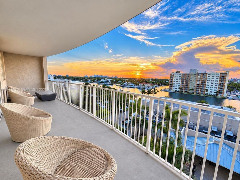 Covered balcony with a concrete surface and a white metal railing overlooking a waterway and urban skyline
