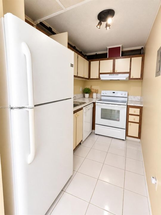 Kitchen featuring white appliances, cabinetry with contrasting trim, stone-patterned countertops, and ceramic tile flooring