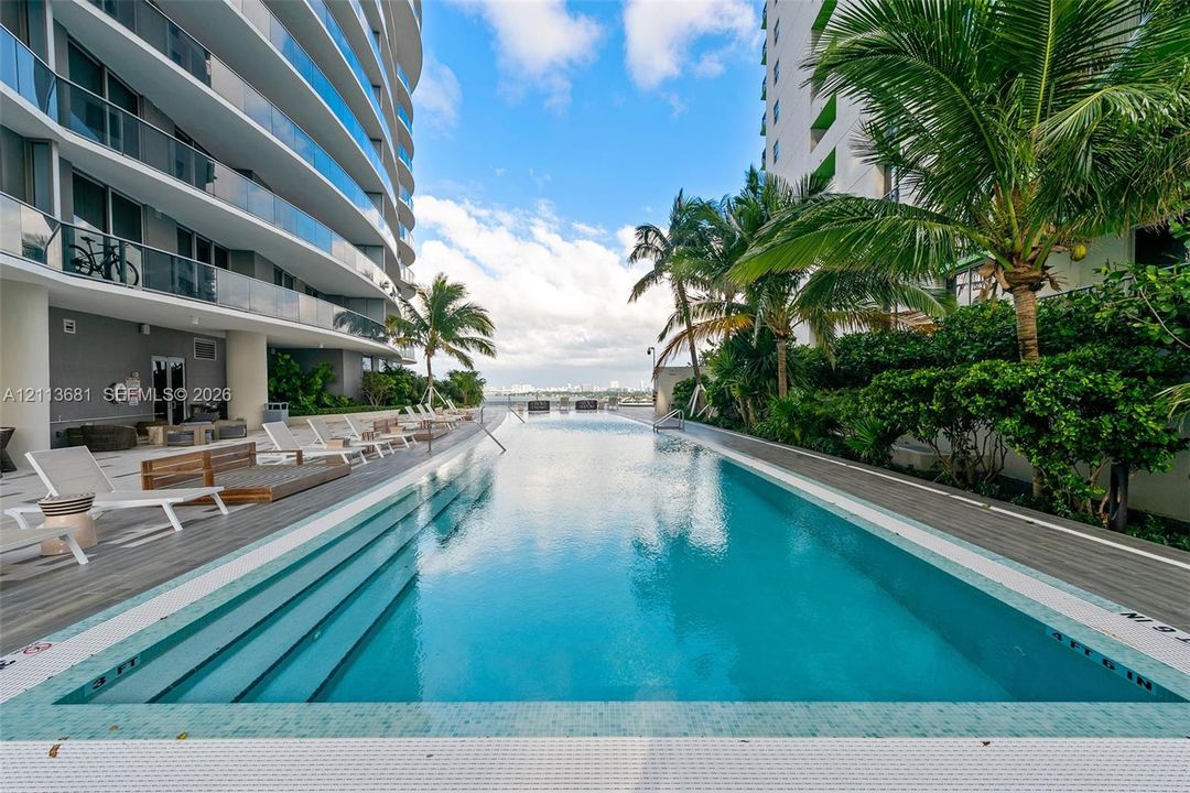 Linear swimming pool featuring integrated steps, tile surround, wood-finish decking, and palm tree landscaping