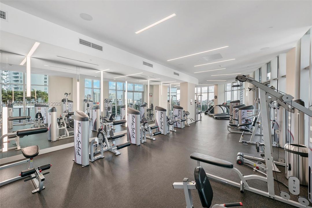 Fitness room featuring floor-to-ceiling windows, mirrored walls, recessed linear lighting, and resilient rubber flooring