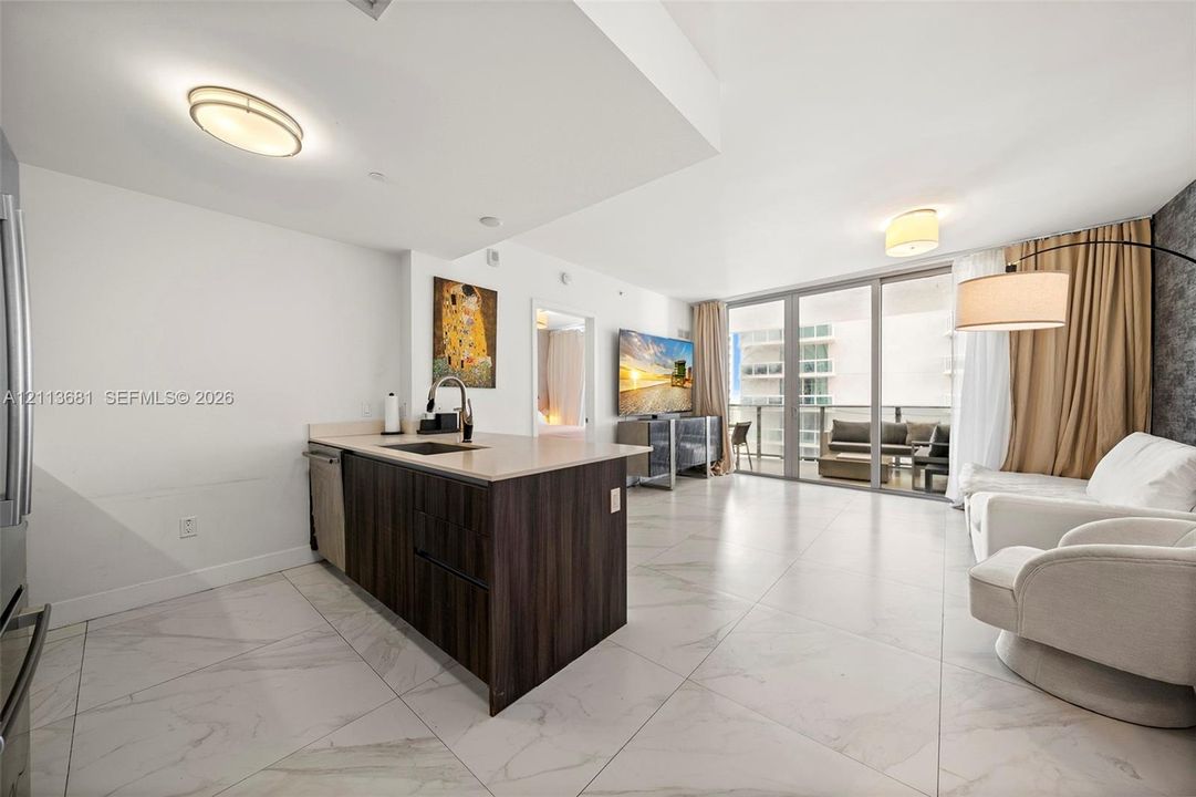 Open-concept kitchen featuring dark wood-finish cabinetry, an island with stone-finish countertops, and large-format tile flooring with stone-pattern detail, complete with floor-to-ceiling glass sliding doors