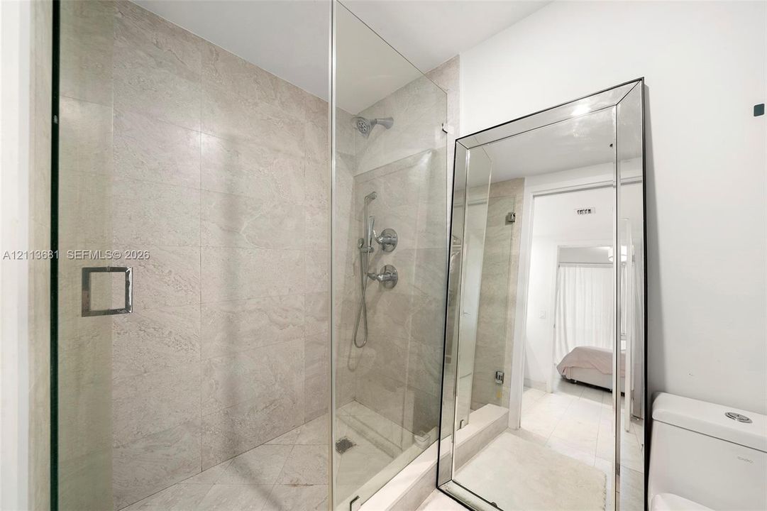 Walk-in shower featuring glass paneling, floor-to-ceiling stone-finish tile, and polished chrome hardware