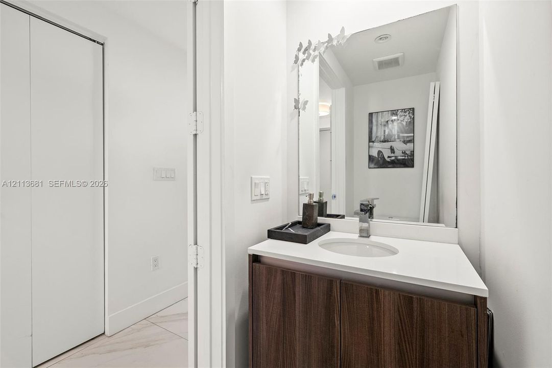 Vanity featuring a wood-finish cabinet, solid surface countertop, integrated oval basin, polished chrome faucet, and floor-to-ceiling mirror