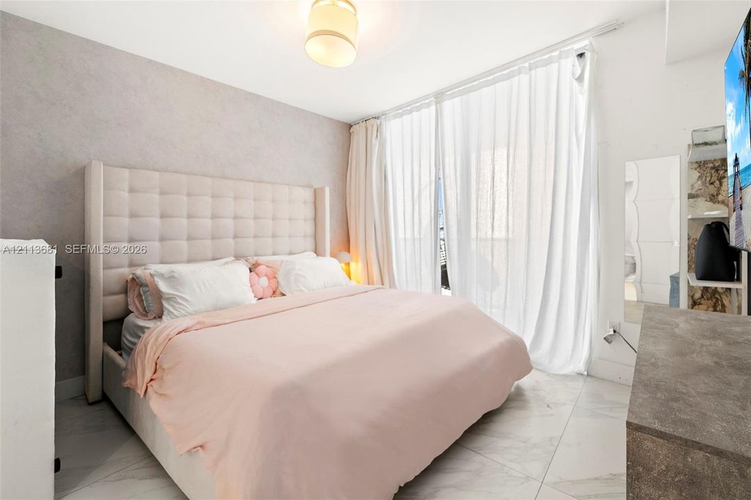 Large-format stone-style flooring, textured accent wall, and floor-to-ceiling glass paneling featuring a neutral-toned drum pendant light fixture