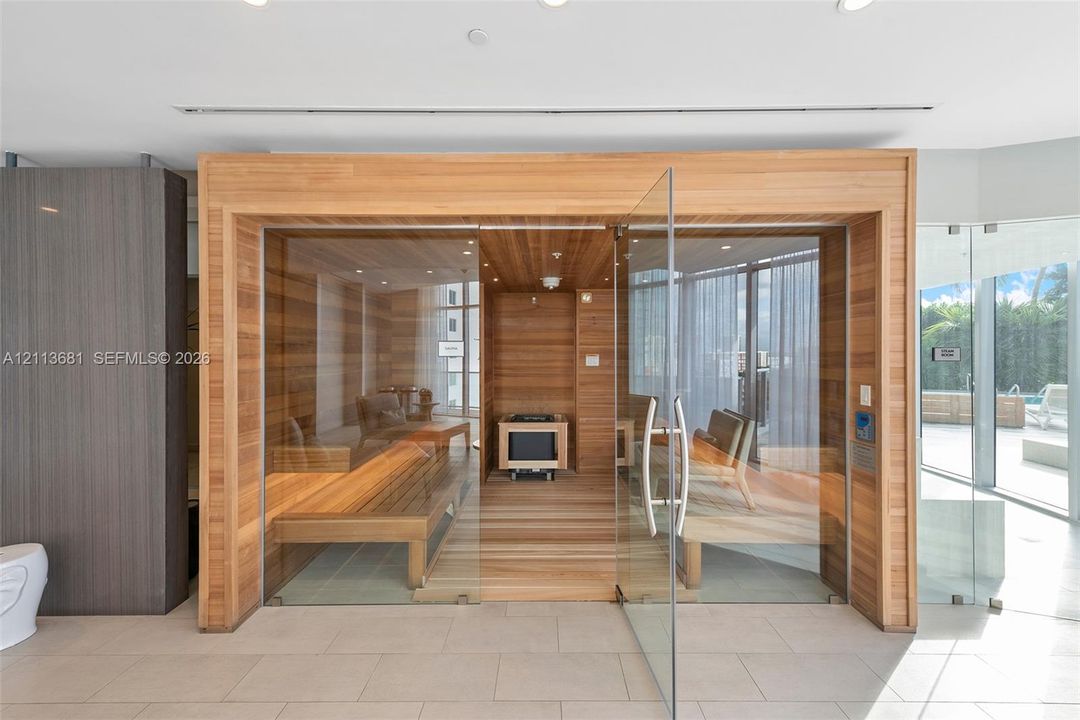 Sauna featuring interior wood paneling, tiered wood bench seating, a mounted heater, and a frameless glass door enclosure