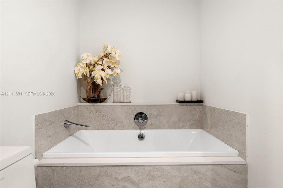Built-in soaking tub featuring large-format stone surround, wall-mounted faucet, and integrated stone deck