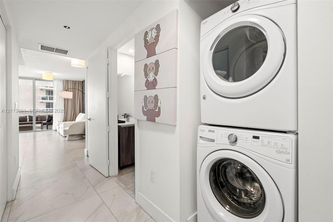 Stacked front-load laundry unit featuring a white finish and large-format porcelain tile flooring