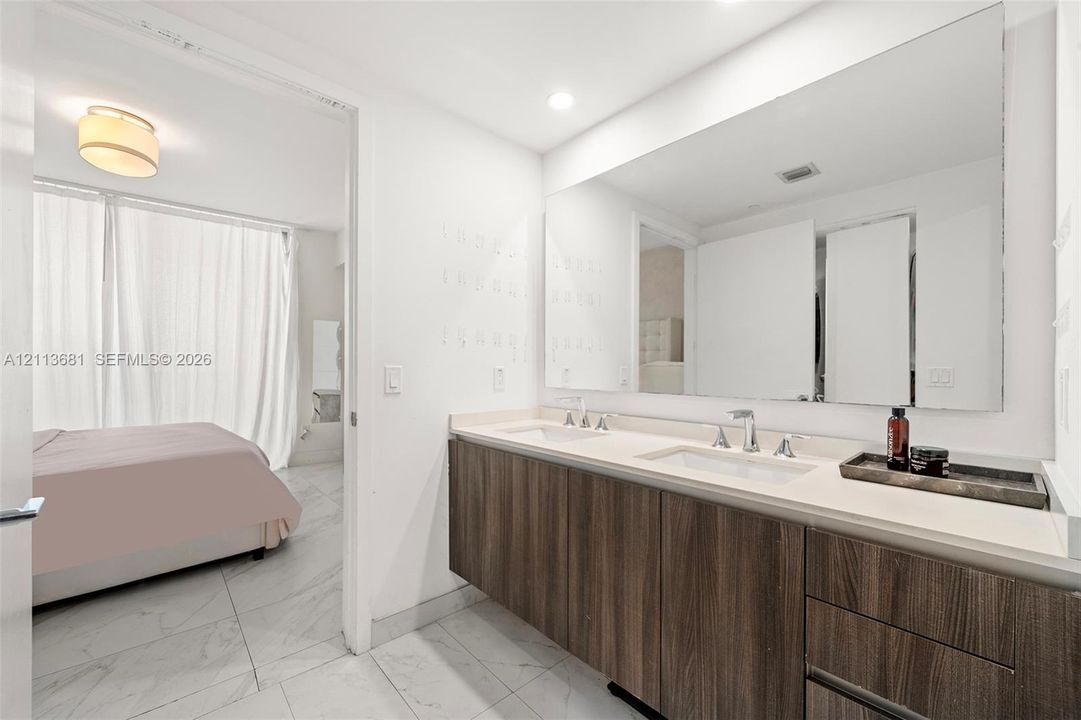 Double vanity with a composite countertop, dual rectangular undermount sinks, wood-finish cabinetry, a large wall-mounted mirror, and light-toned tile flooring