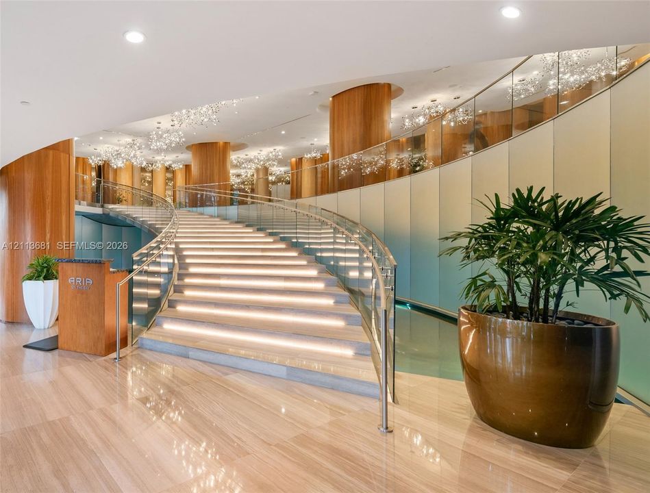 Curved grand staircase with integrated step lighting, wood-paneled pillars, frosted glass wall paneling, and glass railings with metal trim