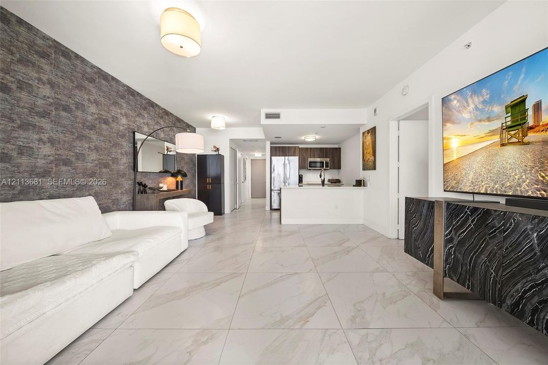 Open-concept interior featuring large-format tile flooring, a textured stone-finish accent wall, and recessed lighting