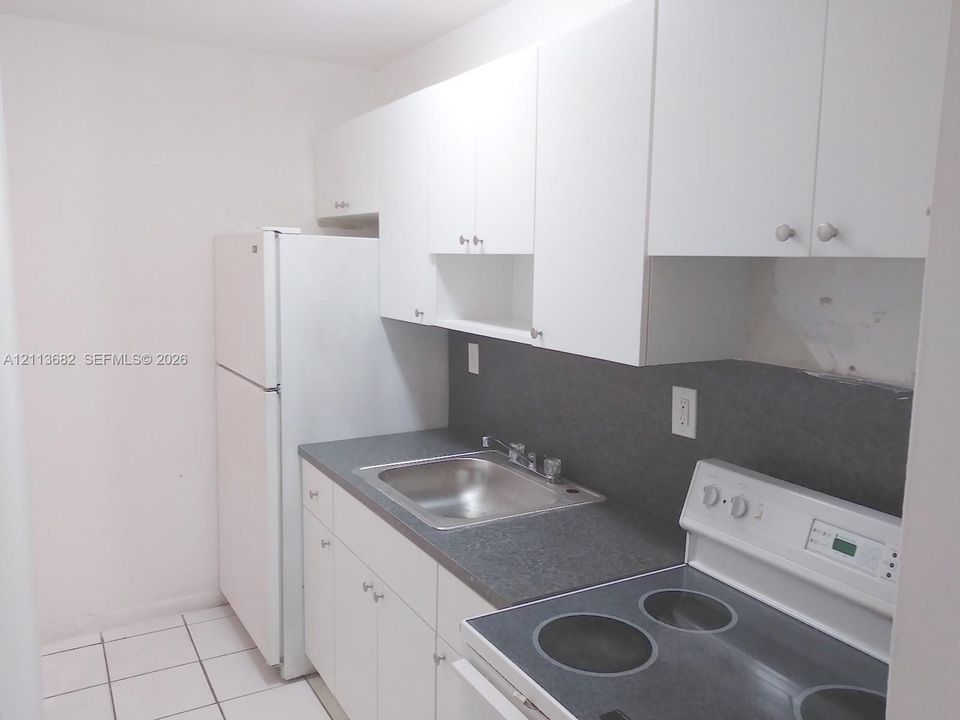 Kitchen featuring white cabinetry, dark solid-surface countertops, a stainless steel sink with a metallic faucet, an electric range, and tiled flooring