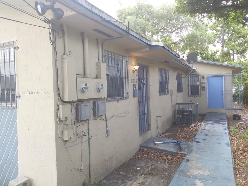 Stucco exterior featuring metal window security bars, concrete walkway, and wall-mounted exterior lighting