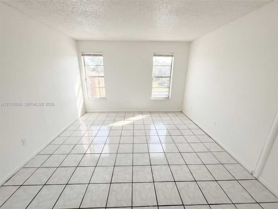 Bright interior room featuring large-format ceramic tile flooring and two windows with white window treatments