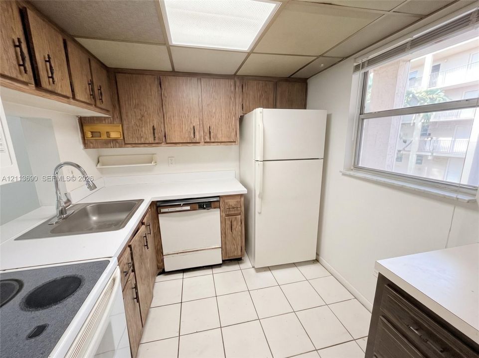 Kitchen featuring wood cabinetry, white solid-surface countertops, a stainless steel sink with a high-arch faucet, white appliances, and tiled flooring