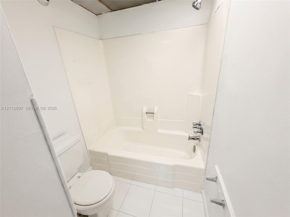 Full-height molded tub surround, porcelain tile flooring, built-in recessed soap dish, chrome finish shower hardware, and high-profile white toilet