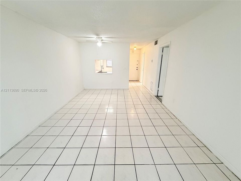 Open-concept room featuring white ceramic tile flooring, a pass-through window, and a ceiling-mounted light fixture