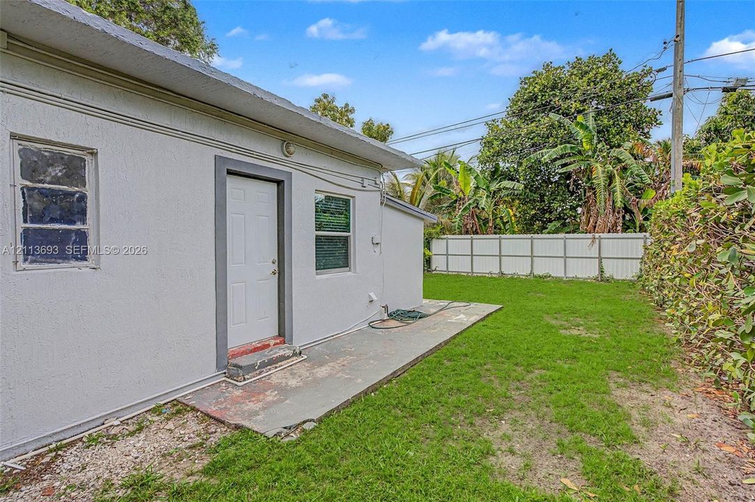 Stucco exterior with a concrete patio, paneled door, and white vinyl privacy fencing