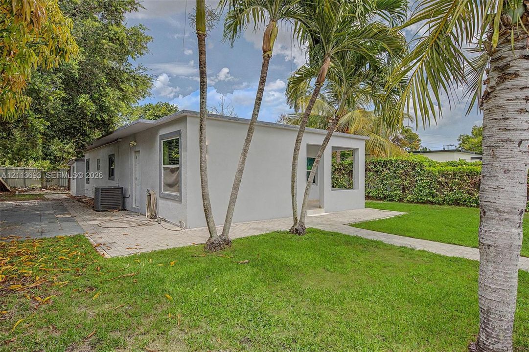 Exterior features including a light-colored stucco facade, a paver patio, a covered entry, established palm trees, and a grass lawn