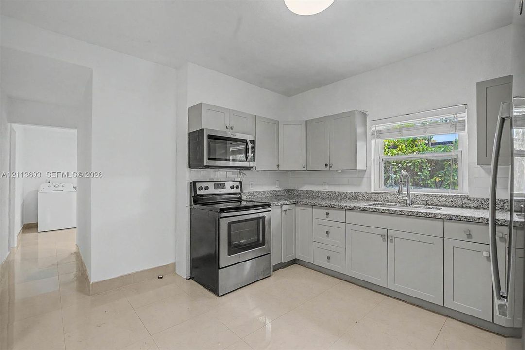Kitchen featuring shaker-style cabinetry, stone-finish countertops, stainless steel appliances, tile flooring, and a single-basin undermount sink with a gooseneck faucet