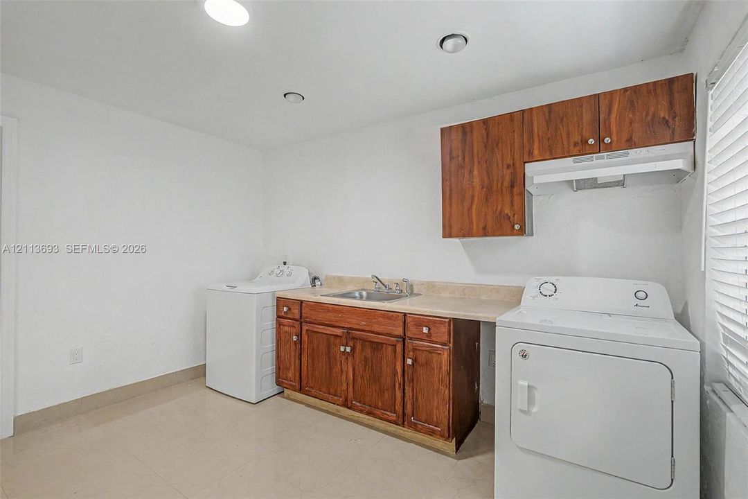Laundry area featuring wood-finish cabinetry, a neutral countertop, an integrated sink with a metal faucet, and recessed lighting