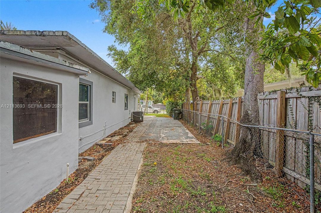 Exterior side yard featuring a paved brick walkway, concrete driveway section, and wood-panel perimeter fencing