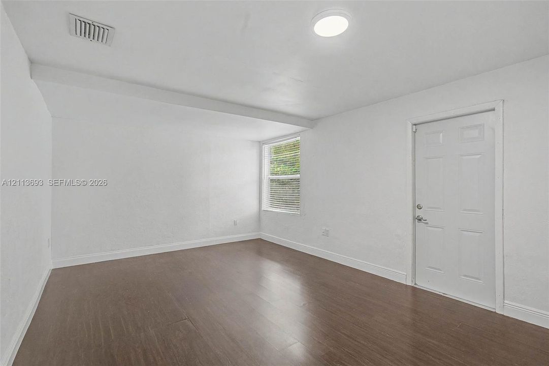 Interior space featuring wood-finish flooring, white walls, a flush-mount ceiling light, and a single-panel door