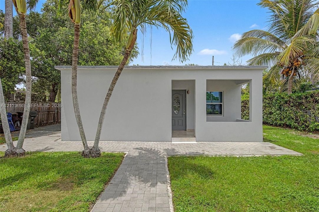 Stucco exterior featuring a recessed front porch, paver walkway, and mature palm trees