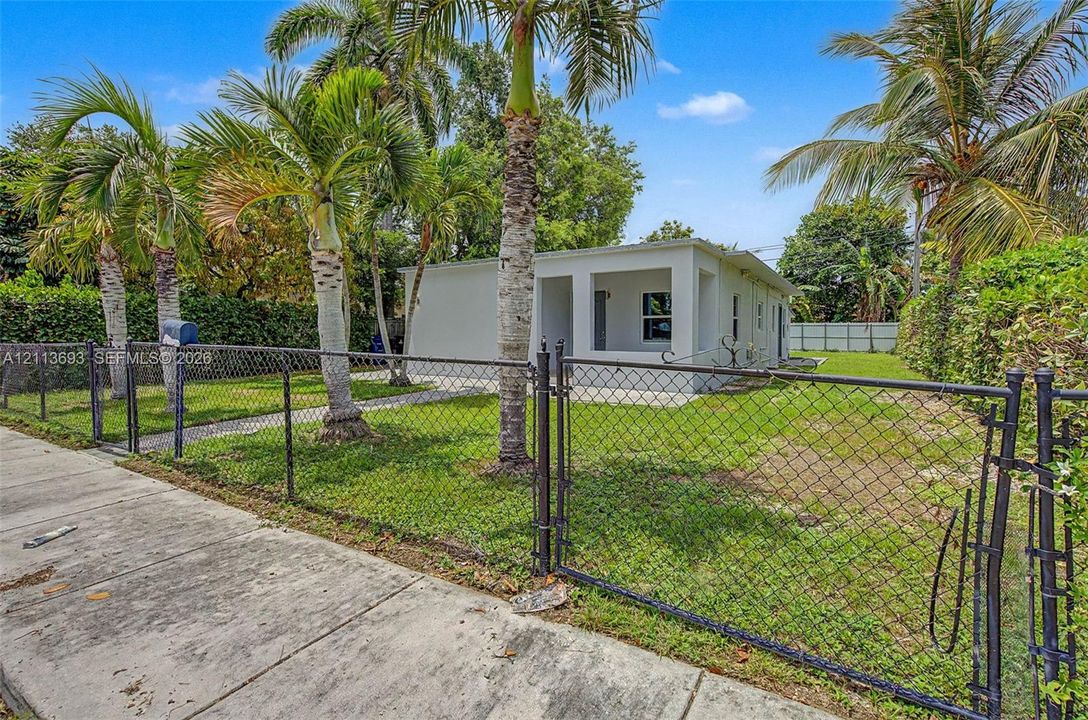 Single-story exterior featuring a covered front porch, fenced yard, and established palm trees