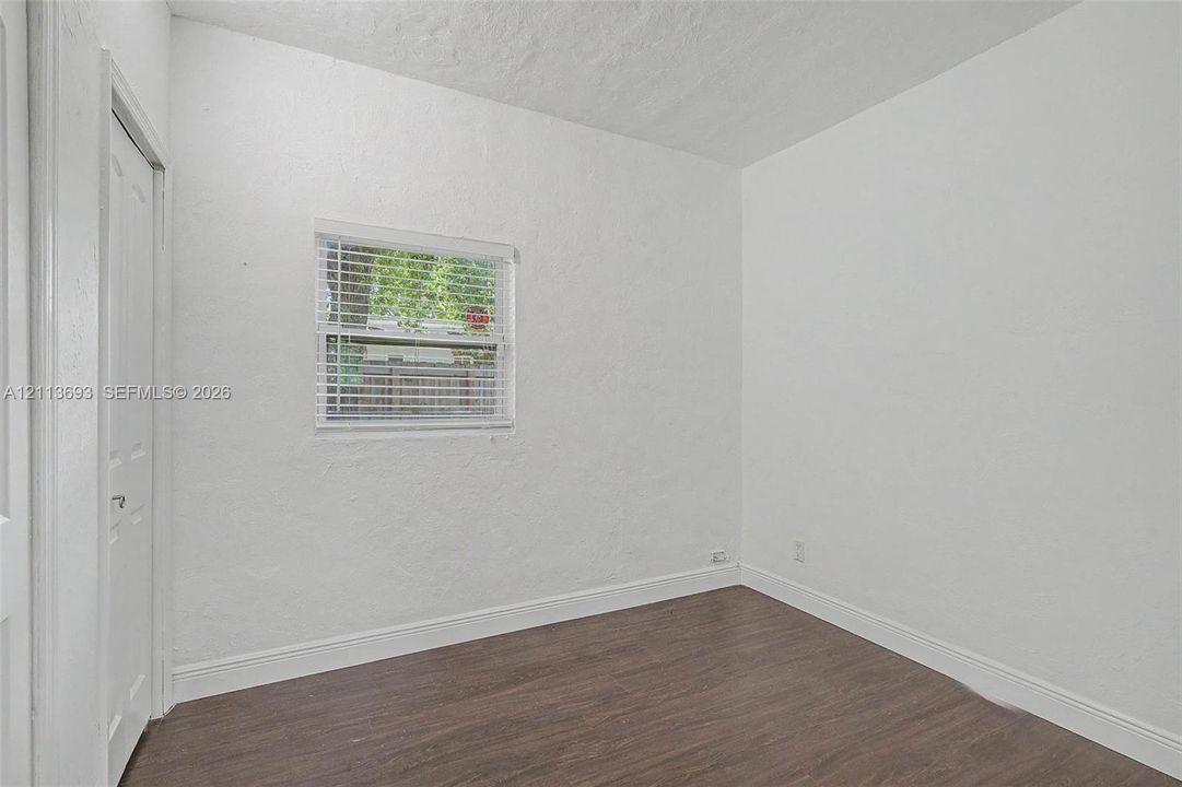 Interior space featuring wood-finish flooring, smooth-textured white walls, and a single-hung window with slatted blinds