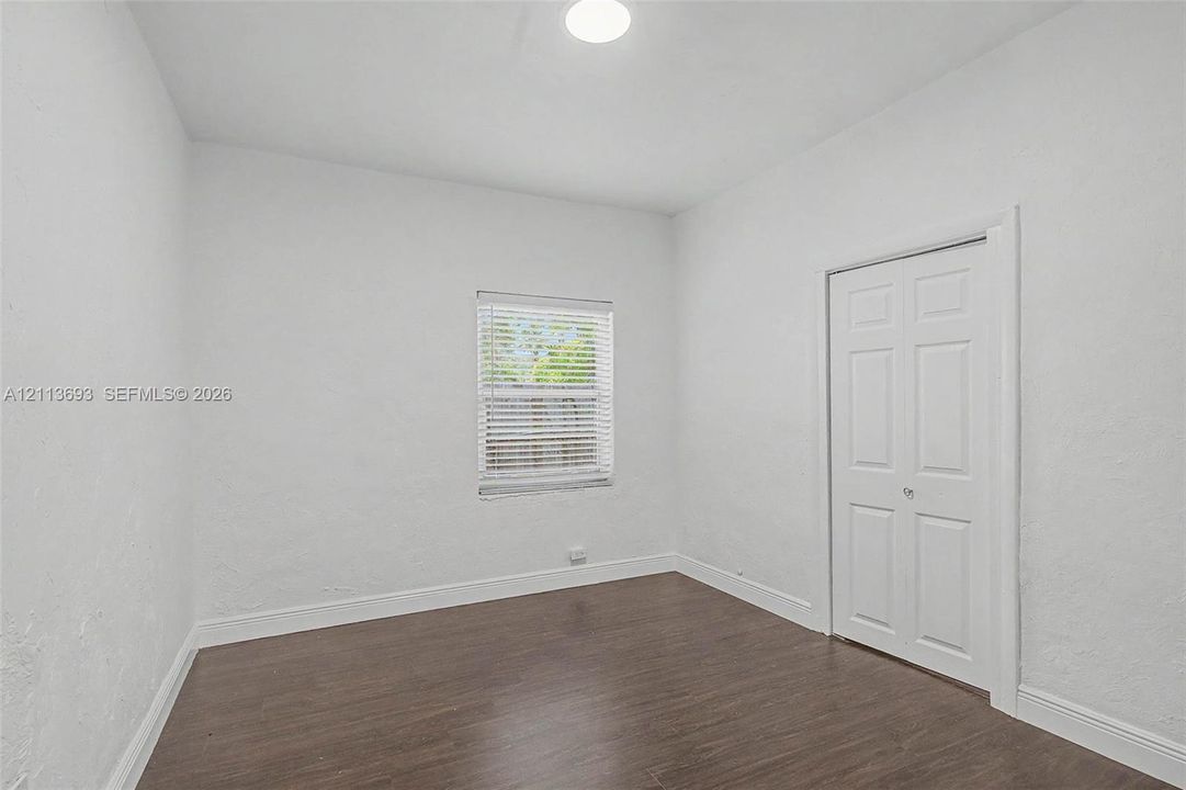 Interior room featuring wood-finish flooring, textured white walls, a single window with horizontal blinds, and a white six-panel bi-fold closet door