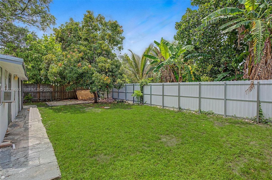Private backyard featuring a manicured lawn, perimeter metal fencing, mature trees, and a concrete patio