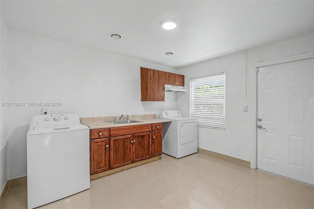 Utility space featuring wood-finish cabinetry, a laminate countertop with an integrated metal sink, recessed lighting, and tile flooring