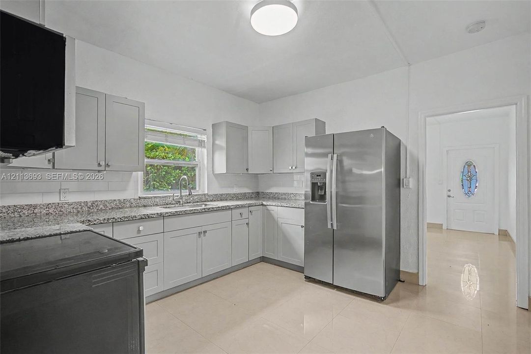 Kitchen featuring light gray cabinetry, stone-finish countertops, stainless steel side-by-side refrigerator, subway tile backsplash, and tile flooring