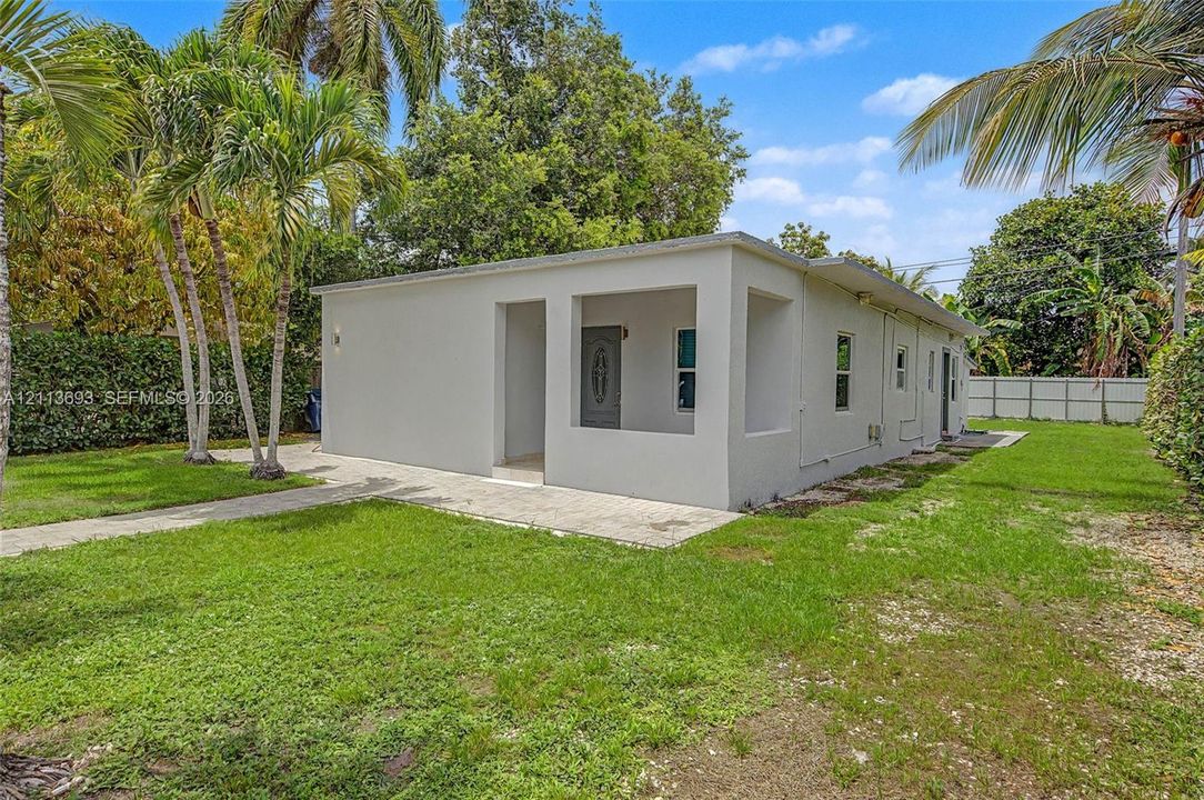 Stucco exterior featuring a covered porch, paved walkway, and surrounding landscaped grounds with mature palms
