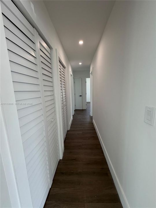 Hallway featuring wood-finish flooring, recessed lighting, and white louvered closet doors