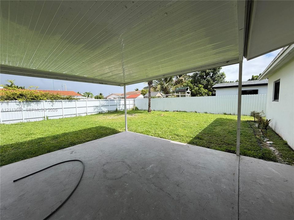 Covered concrete patio with a solid roof structure, expansive fenced backyard, and level lawn