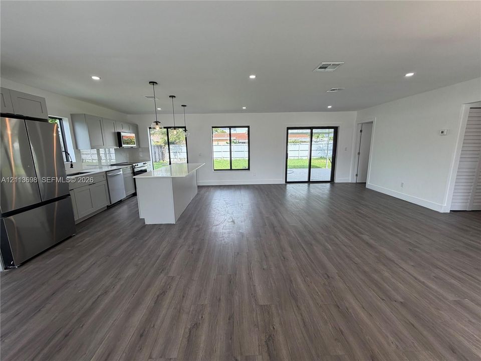 Open-concept kitchen featuring light grey cabinetry, a central island with a solid-surface countertop, stainless steel appliances, recessed lighting, and wood-finish flooring