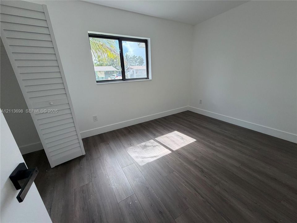 Room featuring wood-finish flooring, a single-panel window with a dark frame, and a louvered-door closet