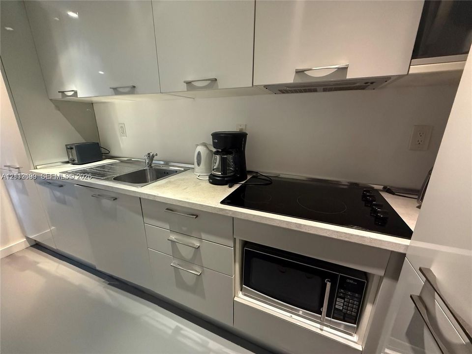 Glossy white cabinetry, stone-finish countertops, stainless steel sink, built-in microwave, and electric cooktop