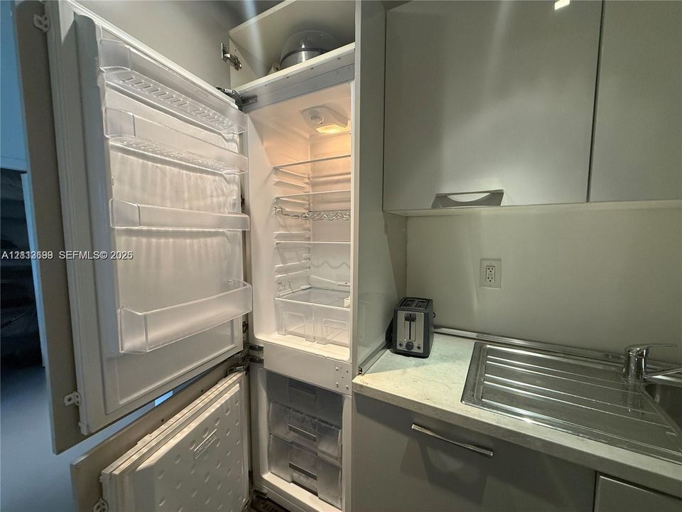 Integrated refrigerator with a cabinet-panel finish, solid-surface countertop, stainless steel sink, and flat-panel cabinetry