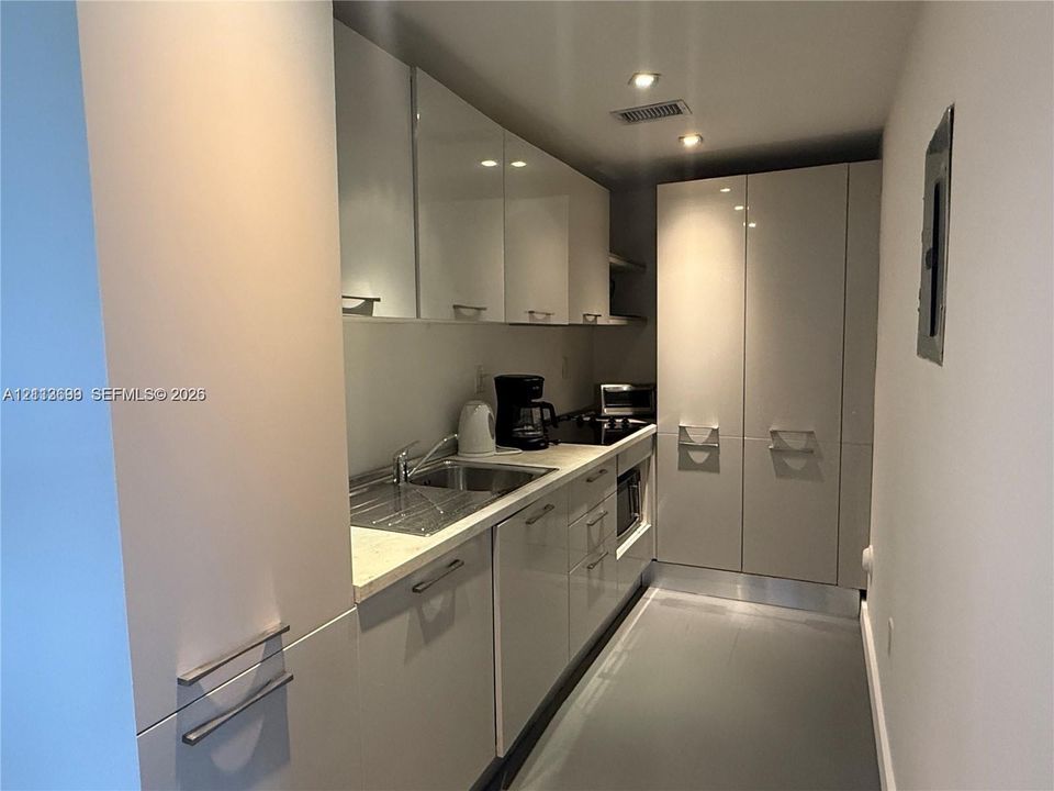 Kitchen featuring high-gloss cabinetry, stone-finish countertops, integrated cooktop, stainless steel sink with metal faucet, and recessed lighting