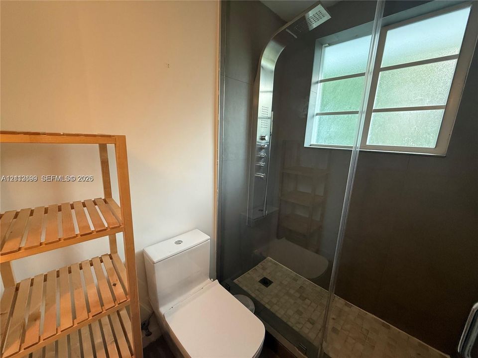 Walk-in shower with integrated stainless steel shower panel, tiled floor, glass enclosure, and opaque window