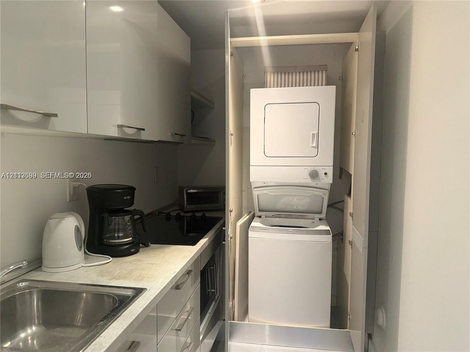 Kitchen featuring high-gloss white cabinetry, integrated cooktop, stainless steel sink, and a built-in laundry closet with a stacked washer and dryer