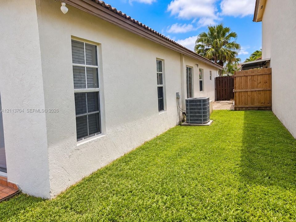 Stucco exterior with multi-pane windows and a side yard featuring a manicured lawn, wood privacy fencing, and exterior HVAC unit