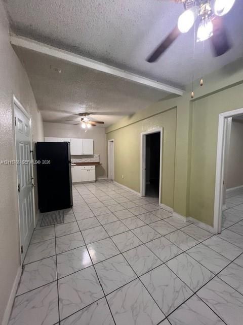 Interior space featuring large-format stone-patterned tile flooring, integrated ceiling fans, and a kitchen area equipped with white cabinetry and a built-in refrigerator