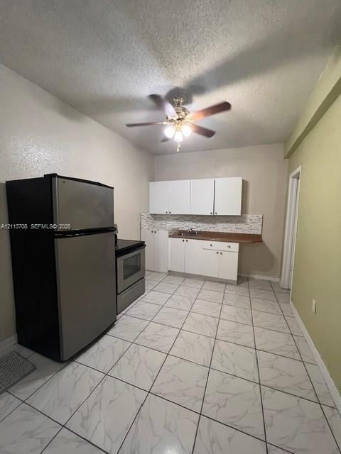 Kitchen featuring white cabinetry, stone-patterned tile flooring, stainless steel refrigerator and range, integrated backsplash, and a ceiling-mounted light fixture with fan