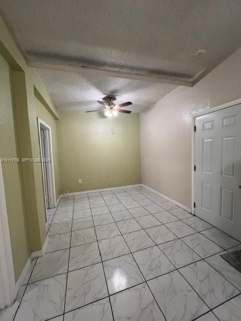 Interior space featuring large-format tile flooring with a marble-style finish, textured ceiling, central ceiling fan with integrated lighting, and a six-panel interior door