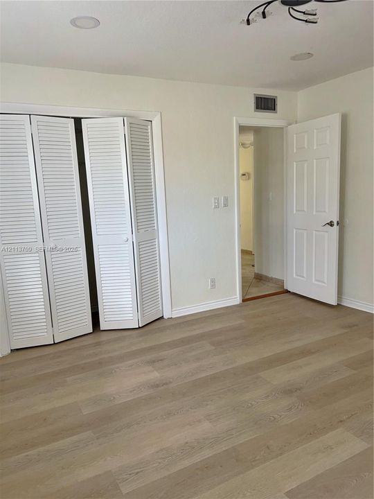 Wood-finish flooring, white louvered bifold closet doors, recessed ceiling lighting, and a six-panel interior door