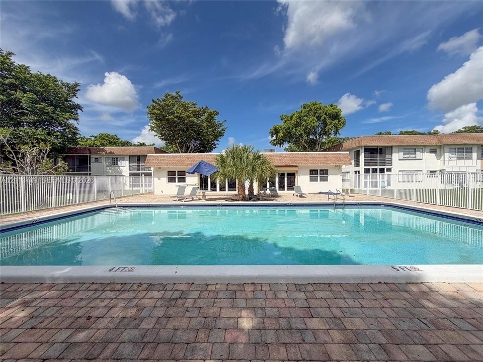 In-ground swimming pool featuring a brick paver deck and white metal fencing